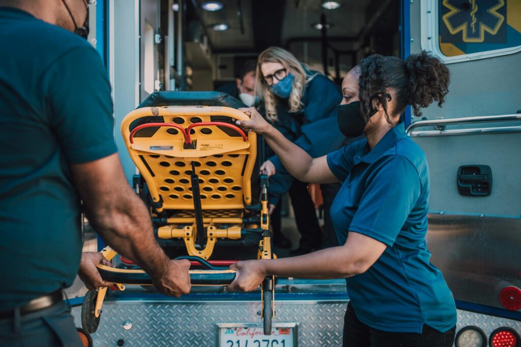 Paramedics wearing masks load a stretcher into an ambulance for emergency medical care.